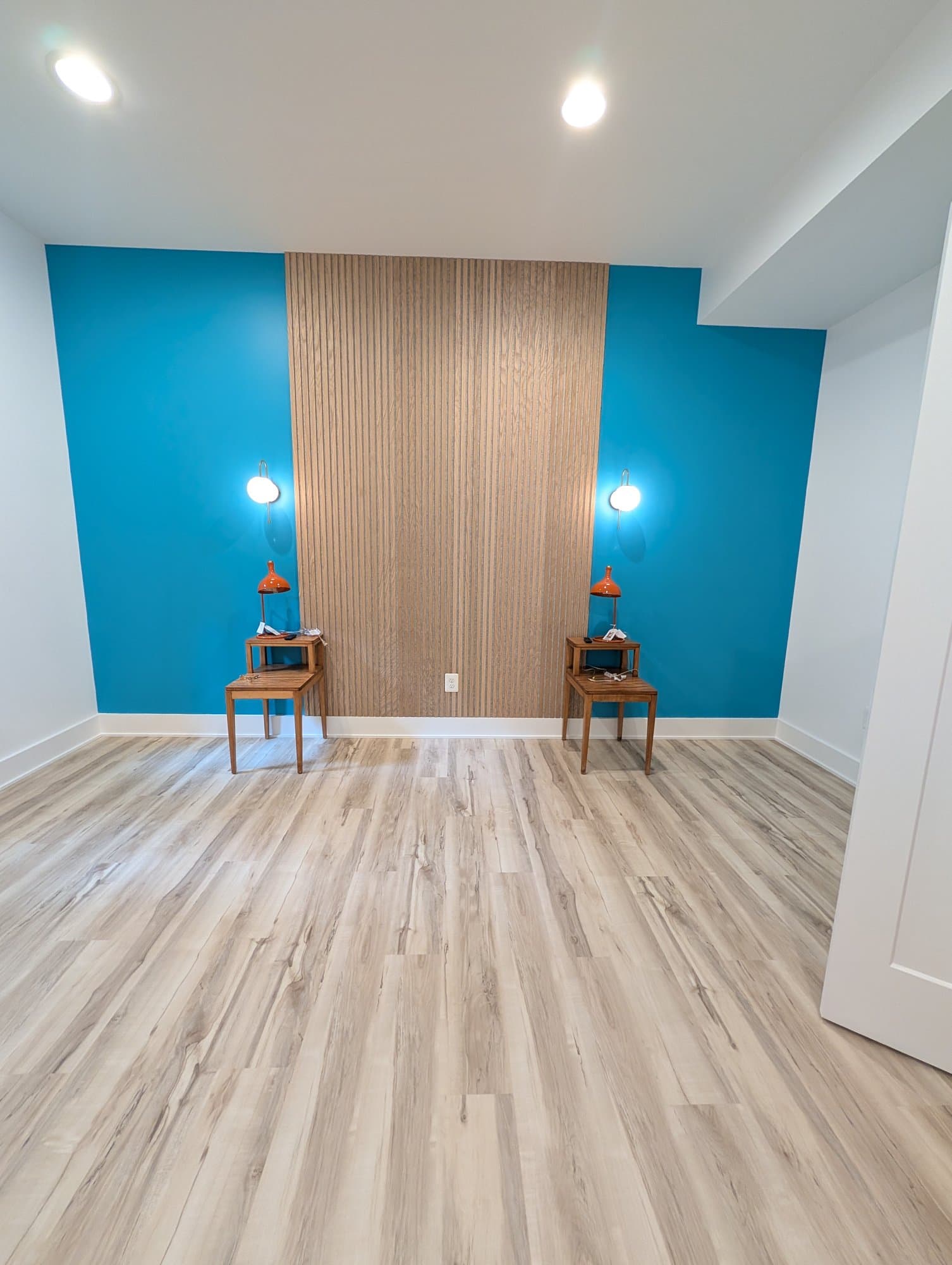 Finished basement room, wide view of the teal accent wall and wood slat panel with matching side tables