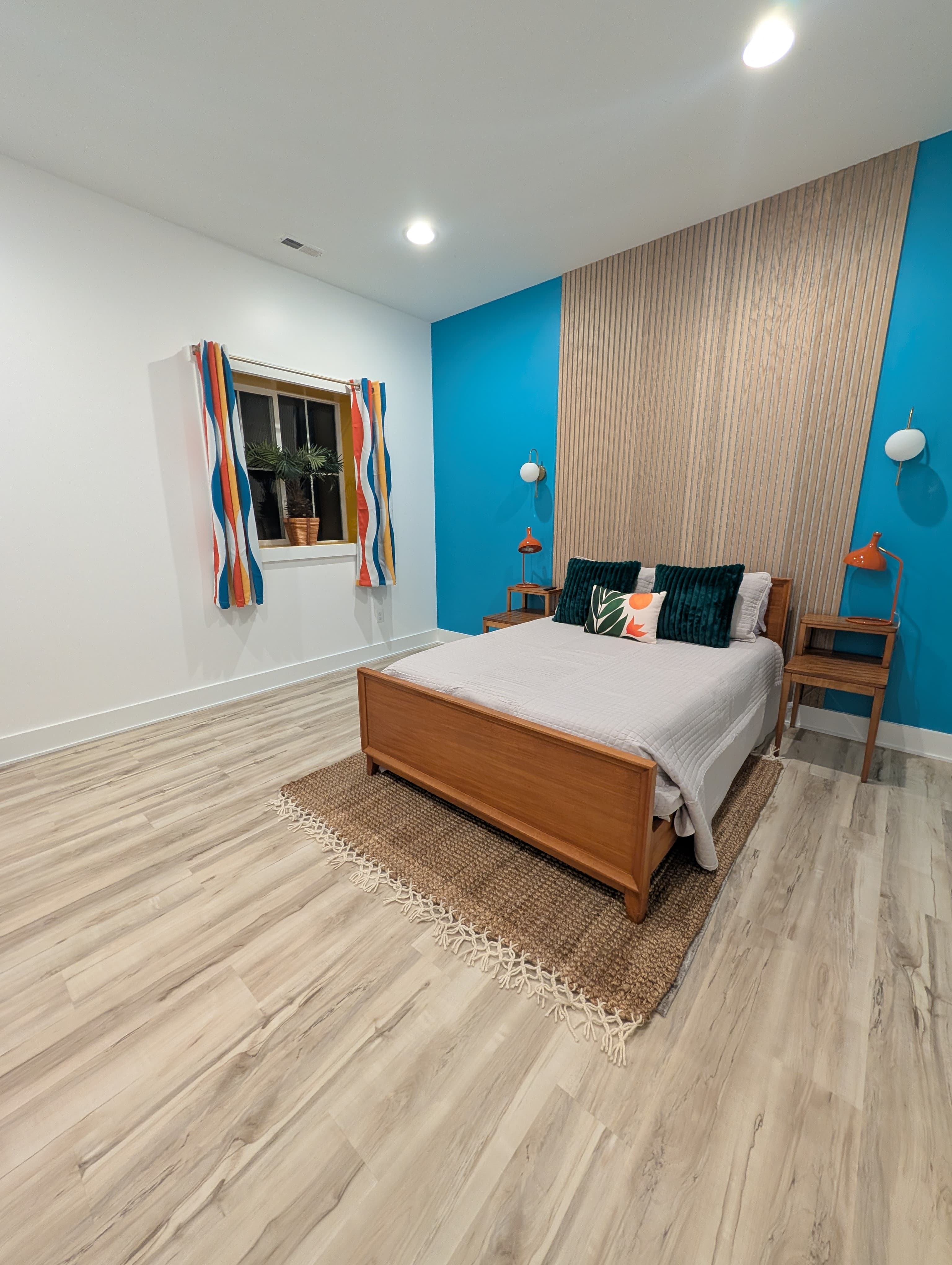Finished basement bedroom, wide view showing a striped curtain over an egress window alongside the teal accent wall